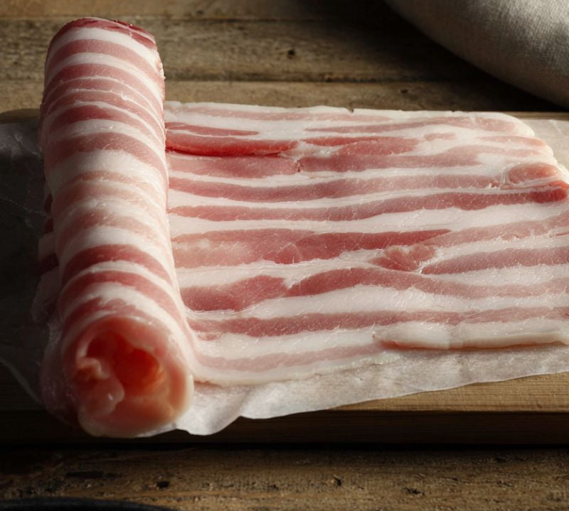 Rashers of British unsmoked streaky bacon on a rustic wooden board — premium rindless pork from The Black Farmer.