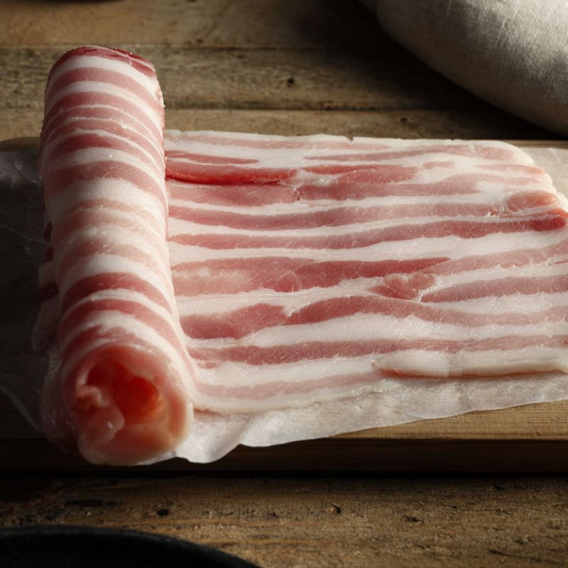 Rashers of British unsmoked streaky bacon on a rustic wooden board — premium rindless pork from The Black Farmer.