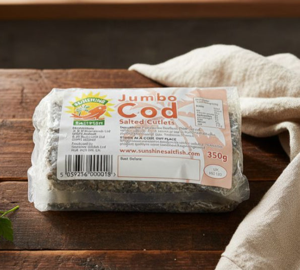Vacuum-packed Sunshine Saltfish Jumbo COD Salted Cutlets 350g on kitchen table beside herbs and salt crystals.
