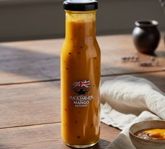 Bottle of Black River Mango Curry Sauce on a wooden table with a bowl and spoon.
