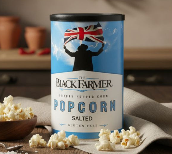 Canister of 'The Black Farmer' salted popcorn on a wooden table with scattered popcorn.