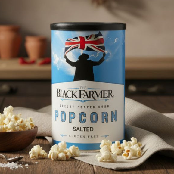 Canister of 'The Black Farmer' salted popcorn on a wooden table with scattered popcorn.
