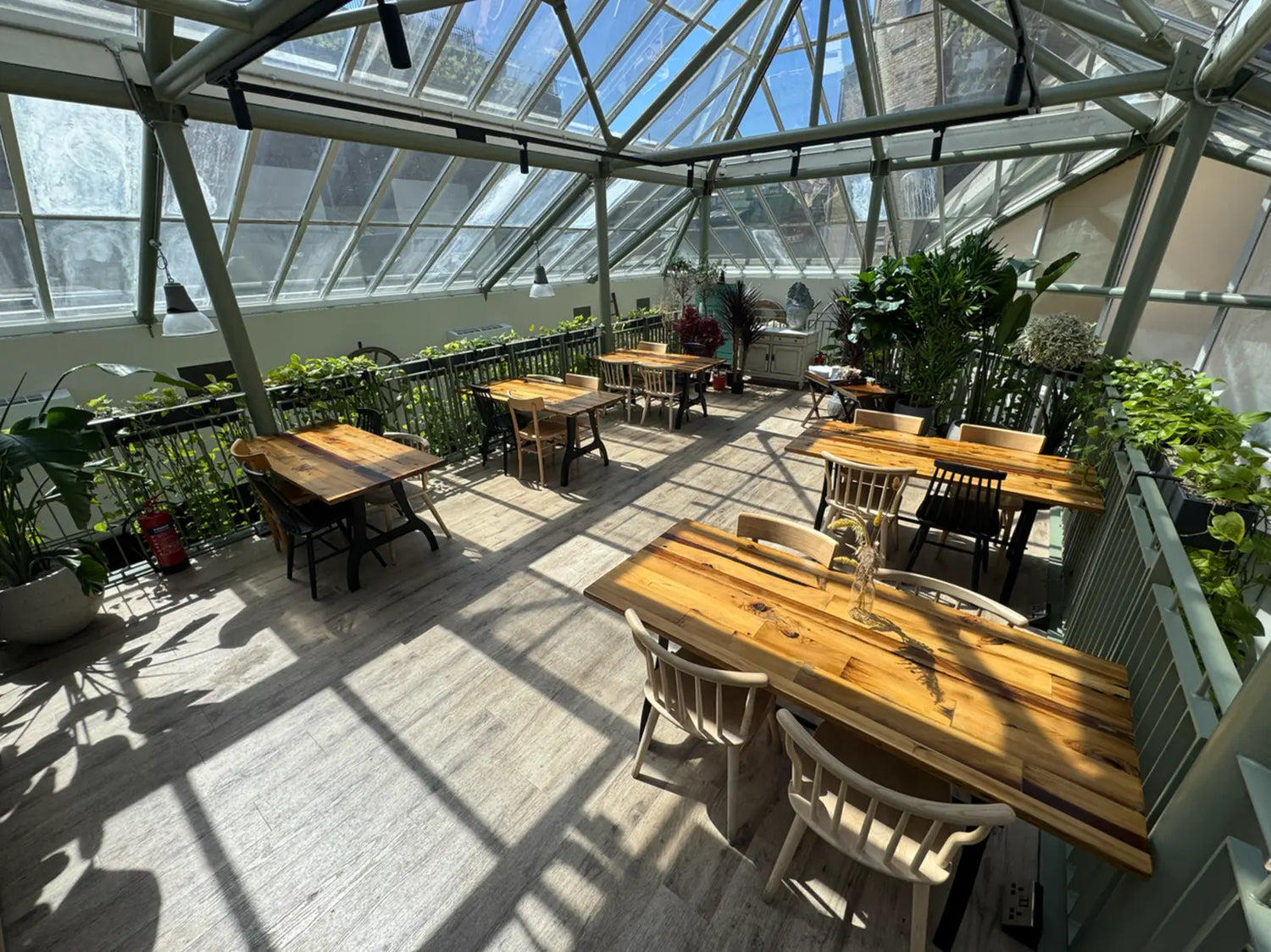 Indoor setting with wooden tables and chairs under a large glass ceiling