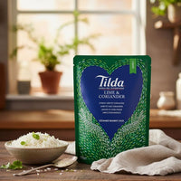 Tilda Lime & Coriander Rice pouch on a wooden kitchen counter with a bowl of fluffy rice