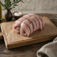Raw turkey breast crown wrapped in bacon on a wooden cutting board with a rustic background.