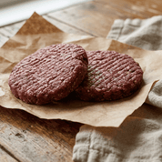 Two raw venison hamburger patties on brown paper with a cloth napkin on a wooden surface
