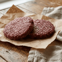 Two raw venison hamburger patties on brown paper with a cloth napkin on a wooden surface