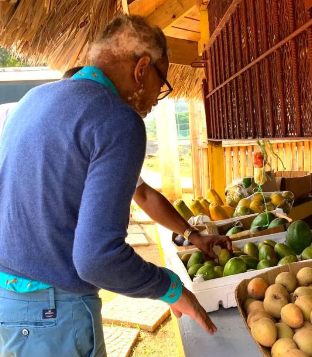 Wilfred sorting fruits in a market setting with a thatched roof