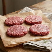 Raw gluten free British beef burgers, 100g patties made with free-range beef, displayed on parchment with herbs