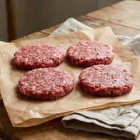 Raw gluten free British beef burgers, 100g patties made with free-range beef, displayed on parchment with herbs