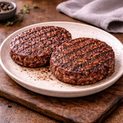 Two grilled goat hamburger patties on a white plate with a wooden background