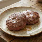 Two cooked patties on a speckled ceramic plate with a wooden background