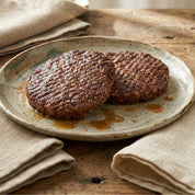Two browned hamburger patties on a rustic ceramic plate with a wooden background.