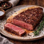 Steak on a plate with a slice cut, surrounded by rosemary and spices.