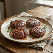 Four grilled beef patties on a ceramic plate with a wooden background
