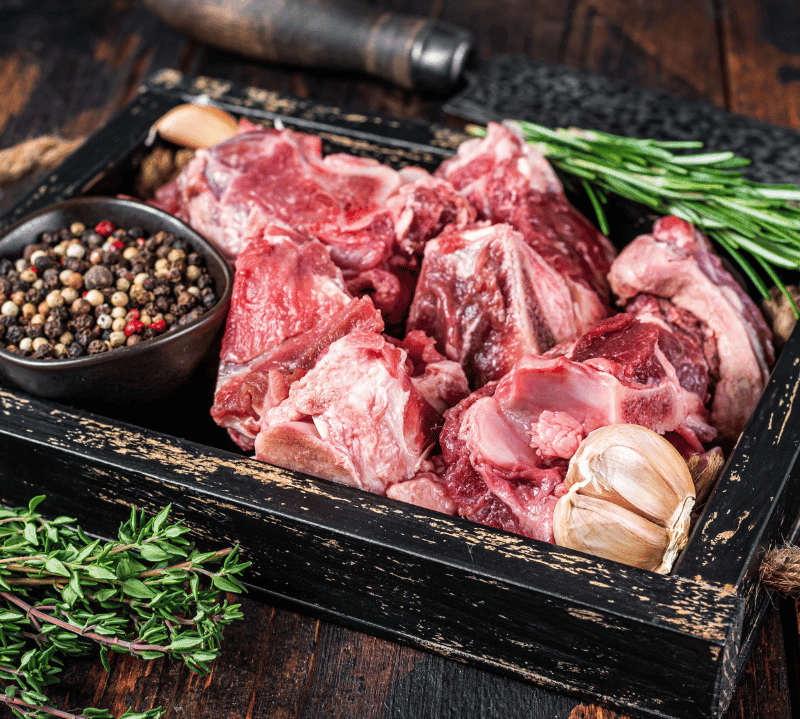 Raw meat chunks on a black tray with herbs and spices on a wooden background