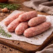 Raw cumberland sausages on a wooden cutting board with herbs and spices.