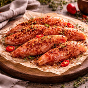 Raw chicken breasts seasoned with spices on a wooden board with herbs and tomatoes.