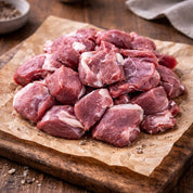 Raw goat chunks on a wooden cutting board with a paper towel underneath.