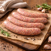 Raw italian sausages on a wooden cutting board with garlic and rosemary.
