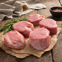 Raw pork fillet medallions on a wooden surface with rosemary and a bowl of spices