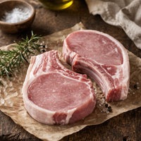 Raw pork chops on a wooden cutting board with rosemary and spices, set against a rustic background.