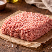 Raw ground pork meat on a wooden cutting board with sage leaves and a cloth in the background
