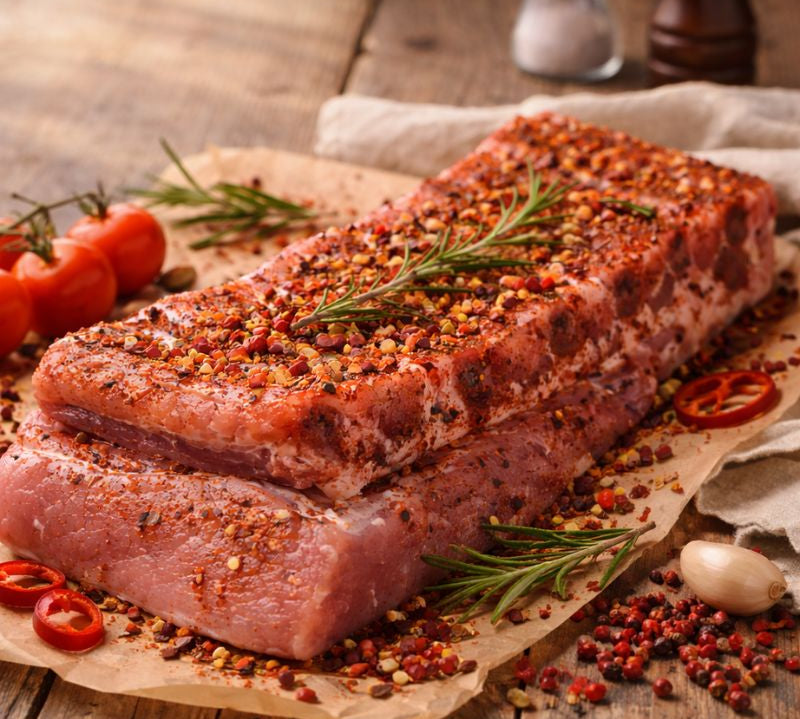 Stack of seasoned raw meat on a wooden cutting board with herbs and salt.