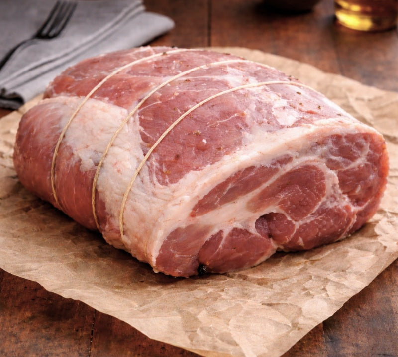 Raw pork shoulder rolled on a wooden surface with rosemary