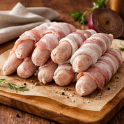 Bacon-wrapped sausages on a wooden cutting board with salt and a knife.