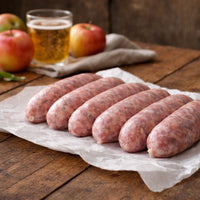 Raw sausages on a wooden board with apples, a glass of beer, and garlic cloves.