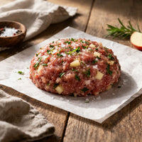 Raw sausage meat patty with herbs on a wooden cutting board