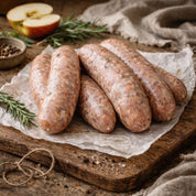 Raw wild boar sausages on a wooden board with apples and herbs
