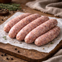 Raw wiltshire sausages on a wooden cutting board with rosemary and salt.