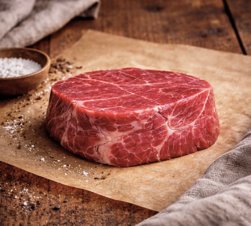 Raw steak on a wooden cutting board with salt and pepper.