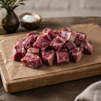Raw mutton chunks on a wooden cutting board with rosemary, on a rustic wooden surface.