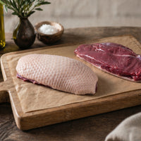 Uncooked British goose breast on a rustic wooden board, seasoned with salt, pepper, and rosemary — premium poultry from The Black Farmer.
